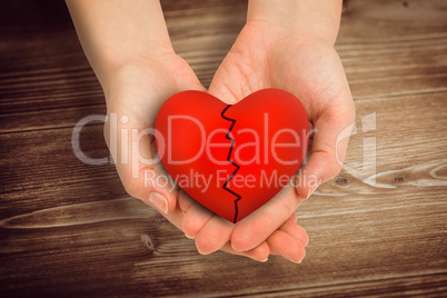 Composite image of couple holding broken heart in hands