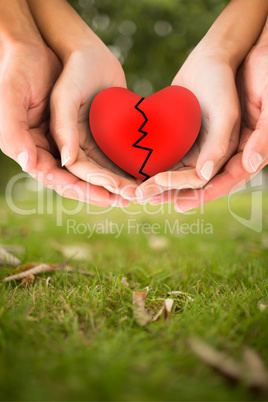 Composite image of couple holding broken heart in hands