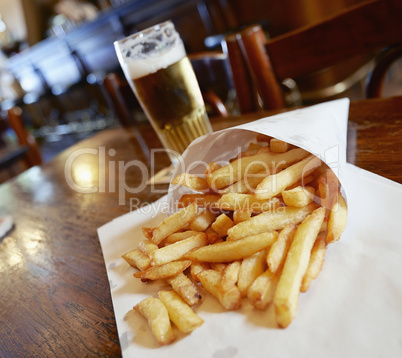 Potatoes fries in a little white paper bag on wood table in brus