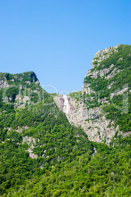 Steep cliffs covered in trees with distant waterfall under blue