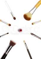 Assorted make up brushes and red lipstick on white background