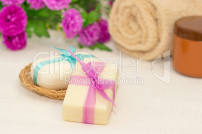 Two pieces of soap with a basket with a bows , flowers , towel a