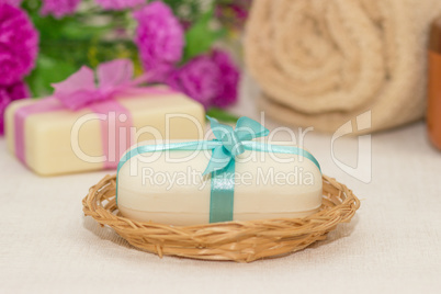 Two pieces of soap with a basket with a bows , flowers , towel a