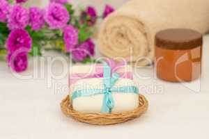 Two pieces of soap with a basket with a bows , flowers , towel a
