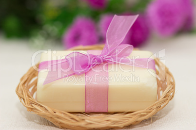 Big piece of beige soap in busket, witn purple bow, flowers on b