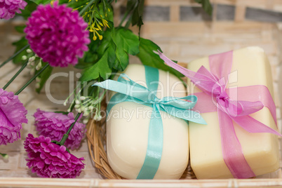 Two soaps with bows in wooden busket with purple flowers
