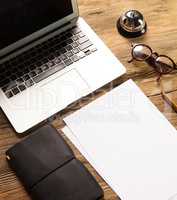 The laptop, blank paper, glasses and small bell on the wooden table