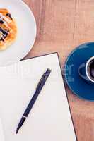 Pen on notepad by food and coffee at table
