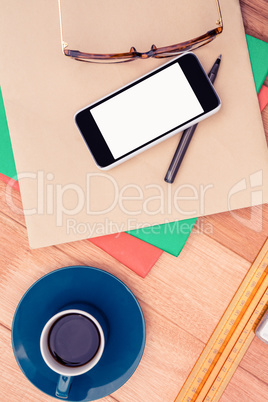 Smartphone and eye glasses on paper by coffee cup at table