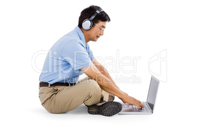 Side view of man listening music while using laptop