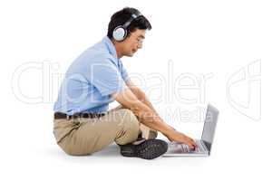Side view of man listening music while using laptop
