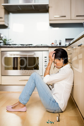 Upset bunette sitting on the floor with bottle of pills