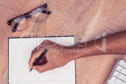 Businessman writing on notebook by eyeglasses at desk