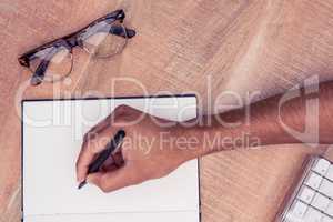 Businessman writing on notebook by eyeglasses at desk