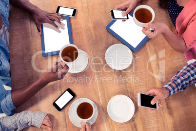 Colleagues using technologies at desk while holding coffee cups