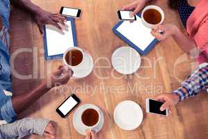 Colleagues using technologies at desk while holding coffee cups