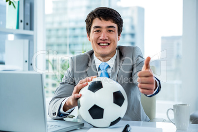 Asian businessman holding soccer ball with thumps up