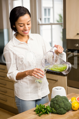 Smiling brunette pouring smoothie in a glass