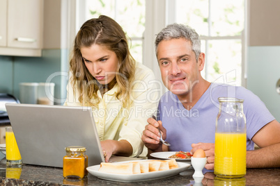 Happy couple using laptop and having breakfast