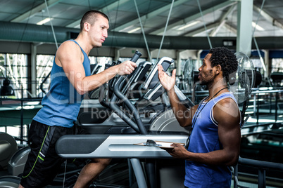 Muscular man using elliptical machine with trainer