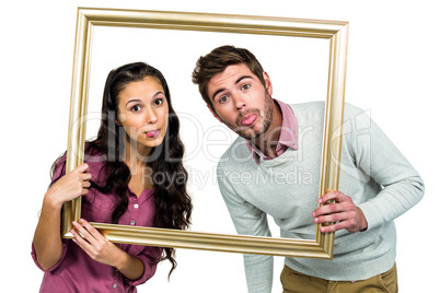Couple sticking out tongue while holding picture frame