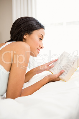 Smiling brunette reading a book on bed