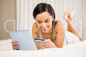 Smiling brunette using tablet and holding credit card