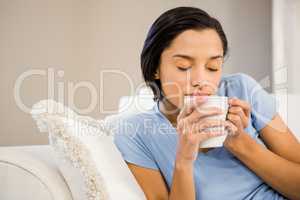 Peaceful brunette drinking by white cup