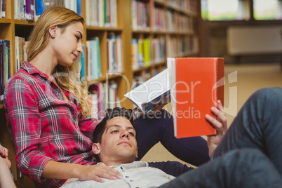 Student reading book while lying on his classmate