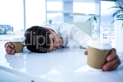 Sleeping businessman holding goblet of coffee