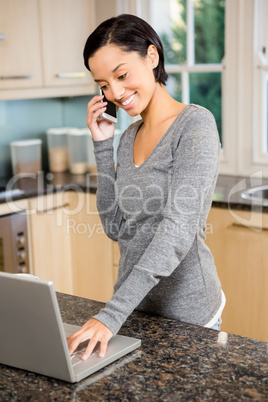 Smiling brunette on a phone call using laptop
