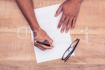 Cropped hand of businessman writing on paper by eye glasses at d
