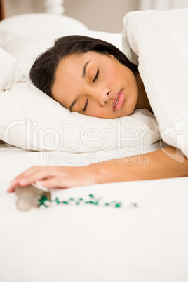 Brunette sleeping in bed by spilt bottle of pills