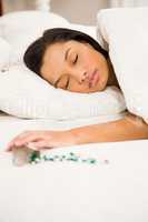 Brunette sleeping in bed by spilt bottle of pills