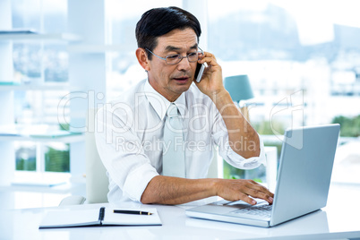 Busy asian businessman working on laptop and calling