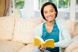 Smiling brunette reading a book on the sofa