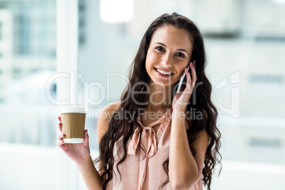 Smiling woman on phone call holding disposable cup