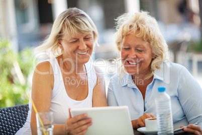 Two women friends using tablet PC in outdoor cafe