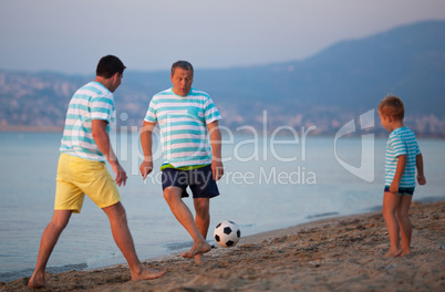 Family team of three playing football at the seaside