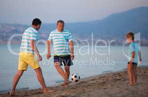 Family team of three playing football at the seaside