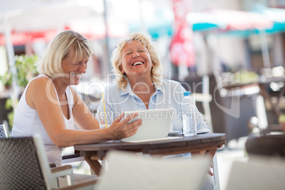 Senior women laughing while using tablet PC in cafe