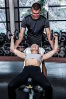 Fit woman doing dumbbells exercise with trainer