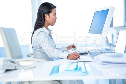 Focused businesswoman taking notes while working on computer