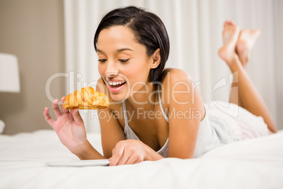 Smiling brunette eating croissant