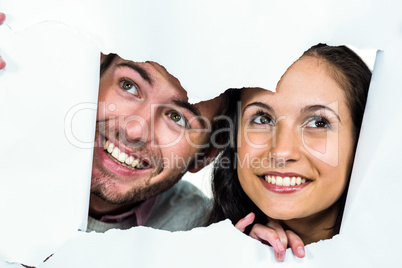 Smiling couple peeking out torn paper
