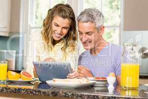 Happy couple using tablet and having breakfast