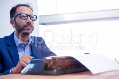 Thoughtful businessman looking away while working on typewriter