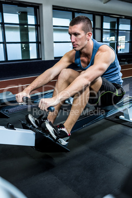 Muscular man using rowing machine