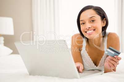 Smiling brunette using laptop and holding credit card