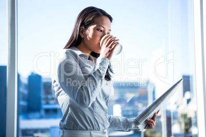 Smiling businesswoman holding disposable cup reading newspaper
